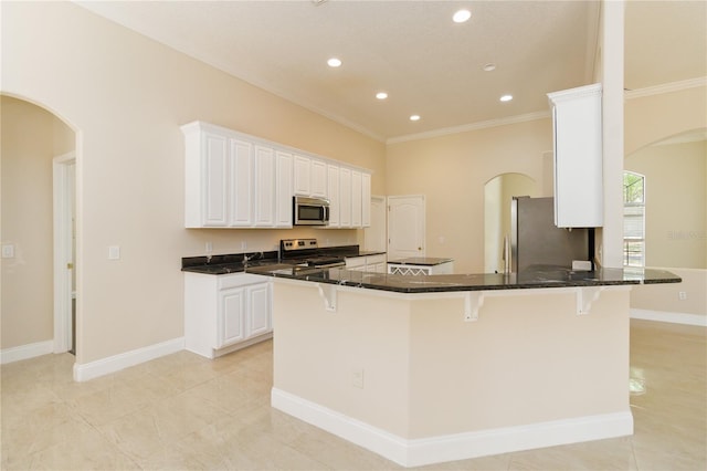 kitchen with crown molding, dark stone counters, stainless steel appliances, white cabinetry, and a kitchen breakfast bar