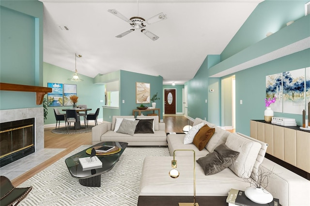 living room with a tile fireplace, light hardwood / wood-style floors, high vaulted ceiling, and ceiling fan