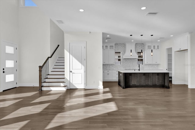 kitchen featuring white cabinets, an island with sink, dark hardwood / wood-style flooring, tasteful backsplash, and decorative light fixtures