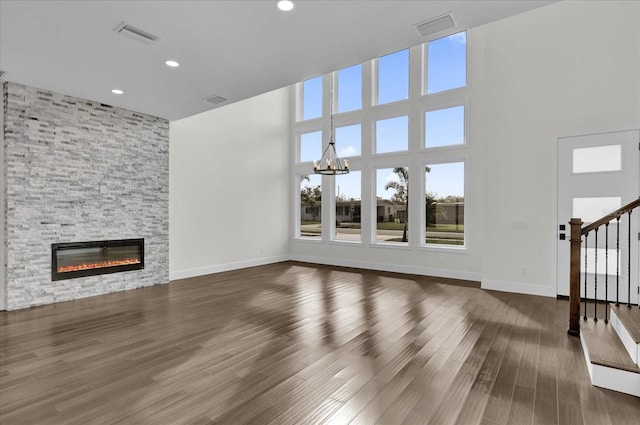 unfurnished living room featuring a fireplace, dark hardwood / wood-style flooring, a chandelier, and a high ceiling