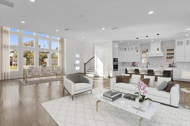 living room with light wood-type flooring, an inviting chandelier, and sink