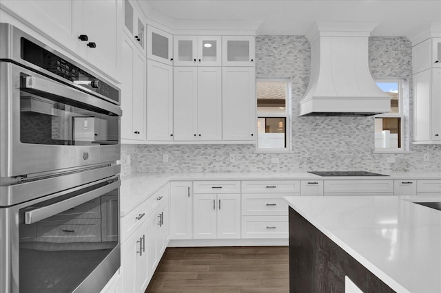 kitchen featuring white cabinets, stainless steel double oven, and premium range hood