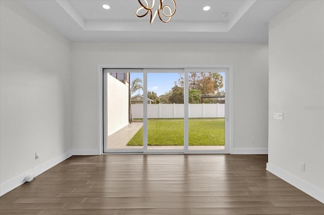 unfurnished room featuring a chandelier, a tray ceiling, and dark hardwood / wood-style flooring