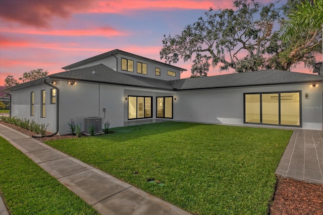 back house at dusk with a lawn and central air condition unit