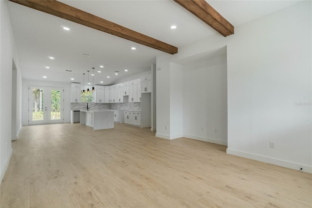 unfurnished living room featuring beam ceiling, light hardwood / wood-style flooring, french doors, and sink