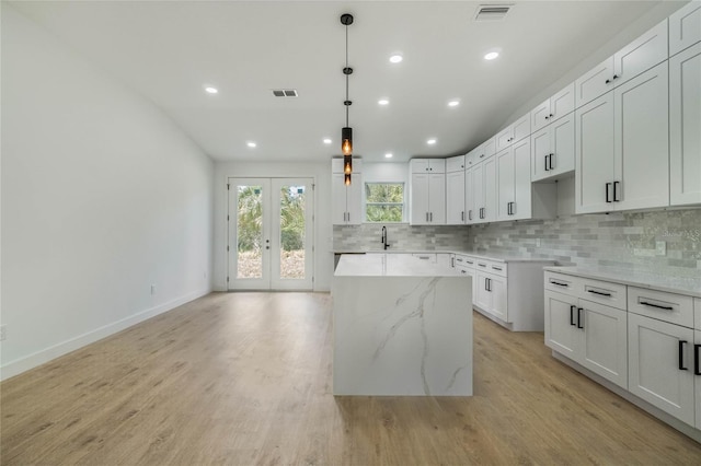 kitchen featuring light stone countertops, sink, white cabinets, a kitchen island, and light wood-type flooring