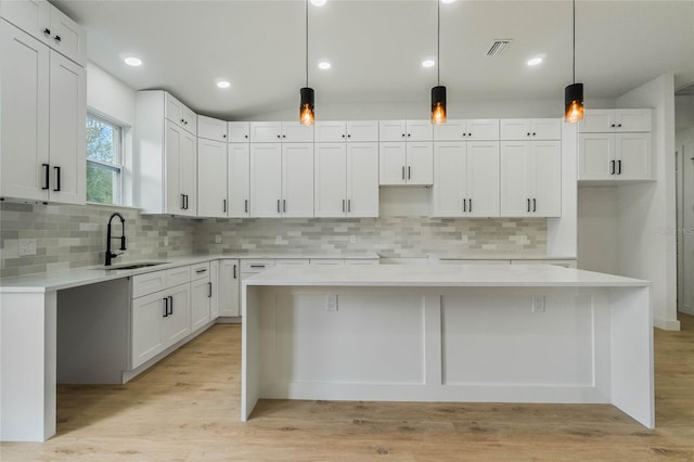 kitchen featuring decorative light fixtures, white cabinetry, sink, and a kitchen island