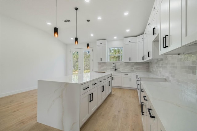 kitchen featuring white cabinets, light wood-type flooring, a kitchen island, and light stone counters