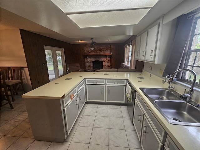 kitchen featuring a fireplace, sink, dishwasher, kitchen peninsula, and ceiling fan