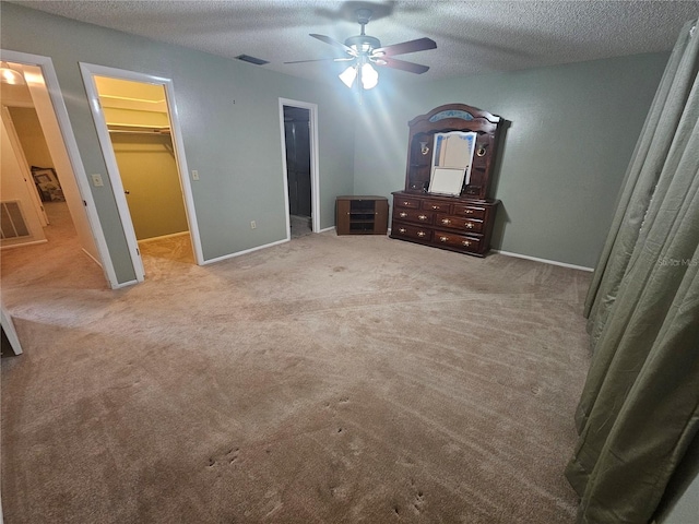 unfurnished bedroom with a textured ceiling, a spacious closet, light carpet, and ceiling fan