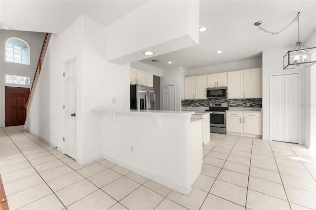 kitchen with hanging light fixtures, stainless steel appliances, tasteful backsplash, kitchen peninsula, and white cabinets