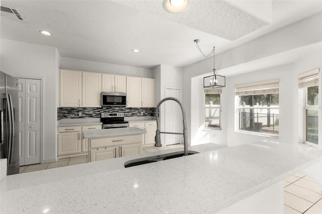 kitchen featuring light stone countertops, stainless steel appliances, sink, light tile patterned floors, and decorative light fixtures