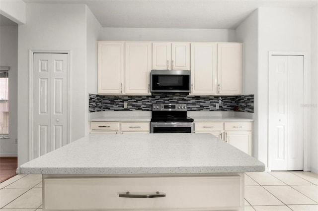 kitchen featuring light stone countertops, tasteful backsplash, light tile patterned flooring, a kitchen island, and appliances with stainless steel finishes