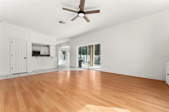 unfurnished living room featuring ceiling fan, sink, and light wood-type flooring