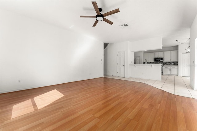 unfurnished living room featuring light hardwood / wood-style flooring, ceiling fan, and sink