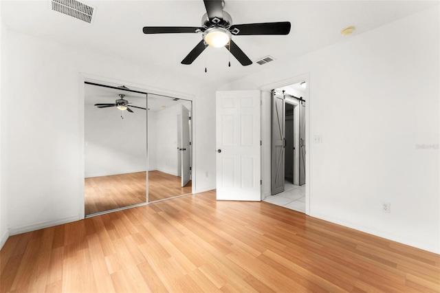 unfurnished bedroom with a barn door, light hardwood / wood-style floors, a closet, and ceiling fan