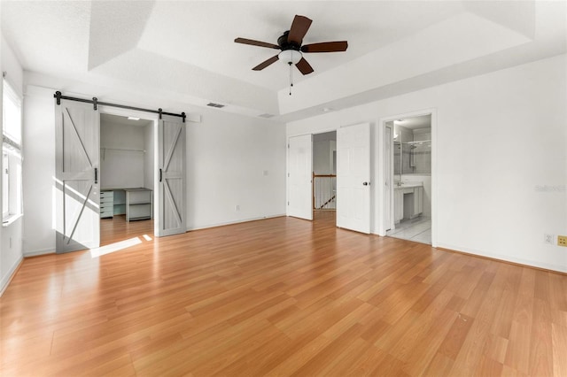 interior space featuring a raised ceiling, a barn door, ceiling fan, and light wood-type flooring