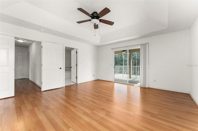 spare room with light wood-type flooring, a tray ceiling, and ceiling fan