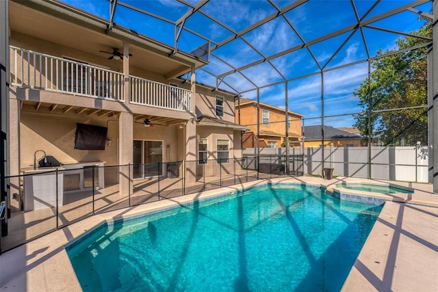 view of swimming pool with glass enclosure, ceiling fan, area for grilling, an in ground hot tub, and a patio