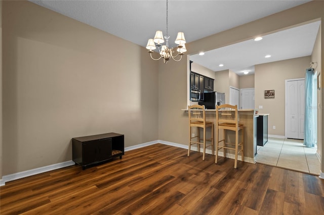 kitchen featuring stainless steel appliances, dark hardwood / wood-style flooring, kitchen peninsula, a chandelier, and a kitchen bar