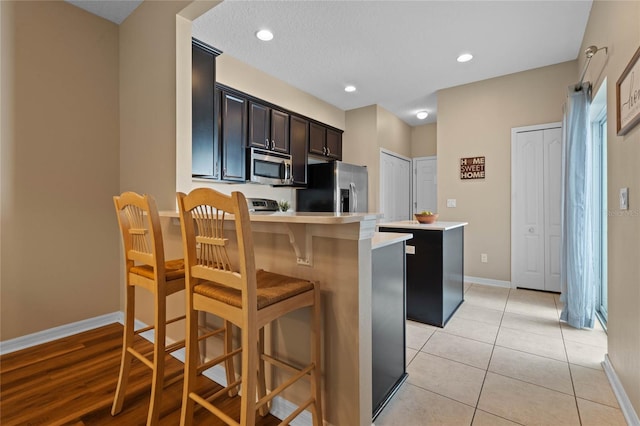 kitchen featuring a center island, a kitchen breakfast bar, a textured ceiling, light tile patterned floors, and appliances with stainless steel finishes