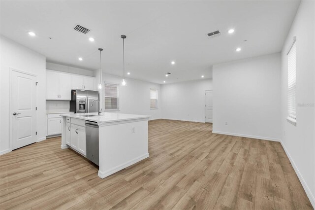 kitchen featuring appliances with stainless steel finishes, pendant lighting, white cabinetry, light hardwood / wood-style floors, and a center island with sink