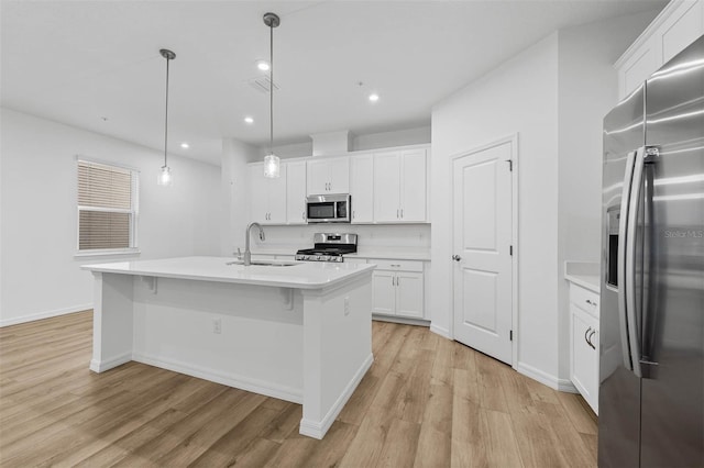 kitchen featuring sink, white cabinetry, hanging light fixtures, stainless steel appliances, and an island with sink