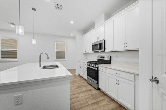 kitchen with white cabinetry, appliances with stainless steel finishes, a kitchen island with sink, and sink