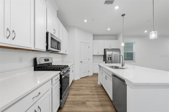 kitchen featuring sink, hanging light fixtures, an island with sink, stainless steel appliances, and white cabinets