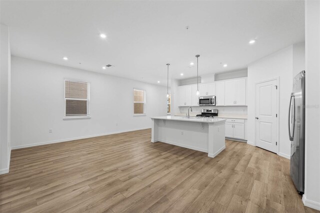 kitchen with pendant lighting, white cabinetry, stainless steel appliances, a center island with sink, and light wood-type flooring