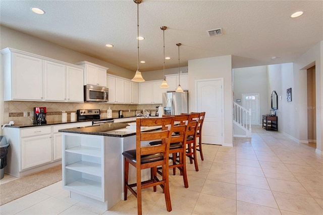 kitchen with hanging light fixtures, a textured ceiling, a kitchen island with sink, white cabinetry, and appliances with stainless steel finishes