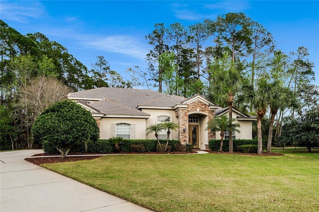 view of front of property featuring a tile roof, stucco siding, stone siding, driveway, and a front lawn