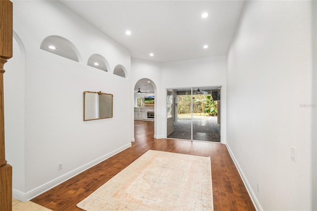 hall with baseboards, arched walkways, and dark wood finished floors