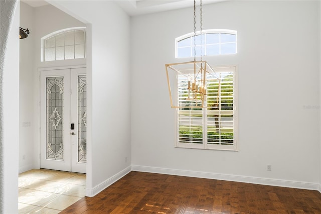 foyer entrance featuring french doors, hardwood / wood-style floors, a high ceiling, a chandelier, and baseboards