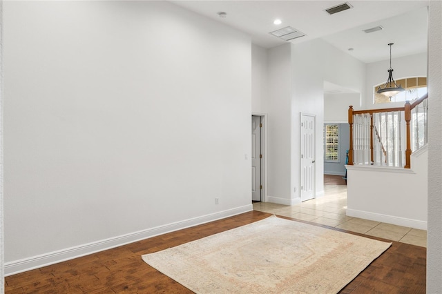 empty room featuring wood finished floors, visible vents, baseboards, and stairs