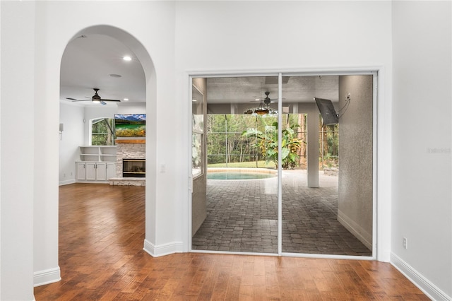 doorway to outside with a stone fireplace, wood-type flooring, a ceiling fan, and baseboards