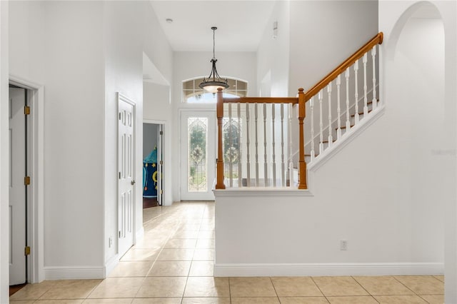 foyer entrance featuring light tile patterned floors, baseboards, arched walkways, stairs, and a high ceiling