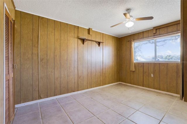 tiled spare room featuring wood walls, ceiling fan, and a textured ceiling