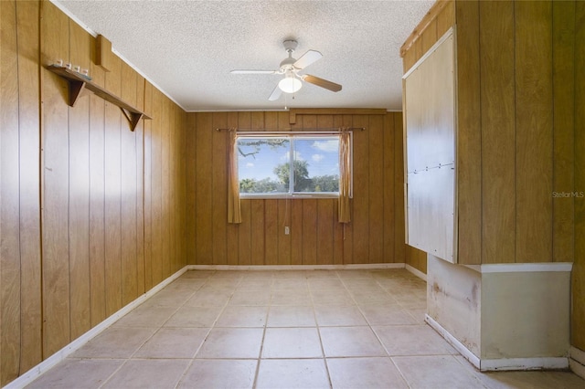 tiled spare room featuring ceiling fan, a textured ceiling, and wooden walls