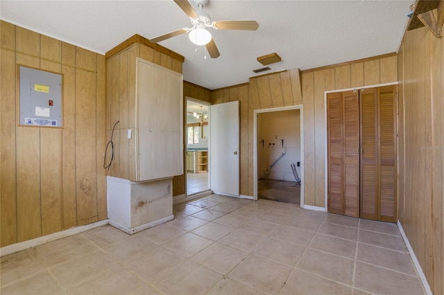 unfurnished bedroom with wood walls, electric panel, ceiling fan with notable chandelier, a textured ceiling, and a closet