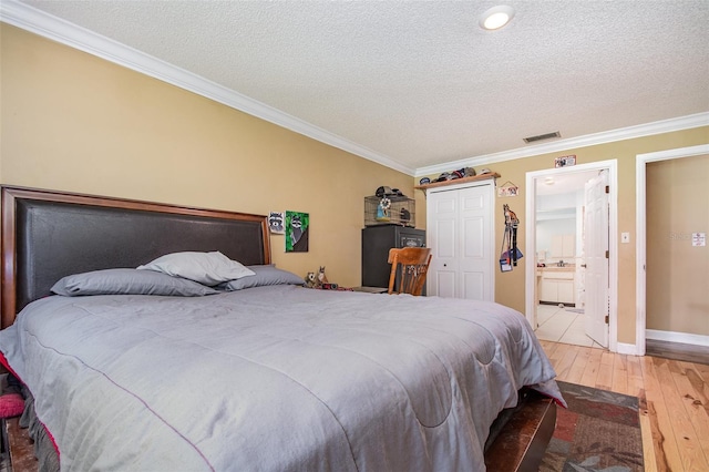 bedroom with light wood-type flooring, a textured ceiling, crown molding, connected bathroom, and a closet