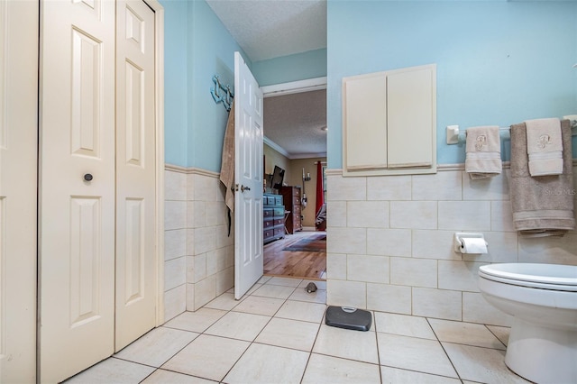 bathroom featuring toilet, a textured ceiling, tile patterned floors, and tile walls