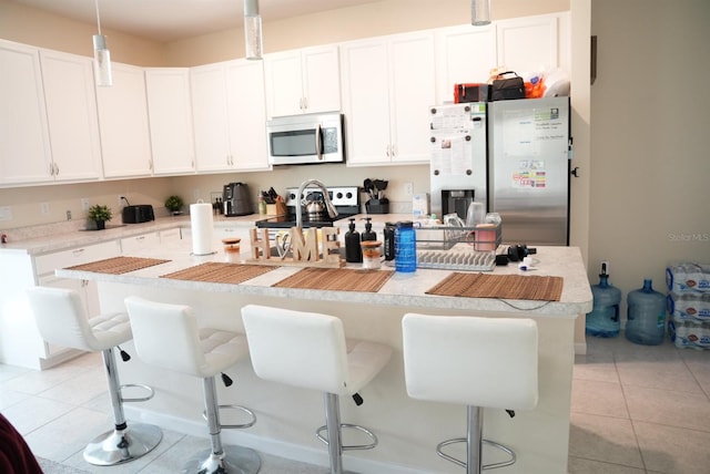 kitchen featuring a kitchen bar, stainless steel appliances, light tile patterned floors, white cabinetry, and decorative light fixtures