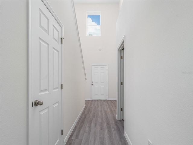 hall featuring a high ceiling, baseboards, and wood finished floors