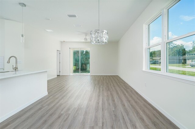 unfurnished dining area with visible vents, baseboards, light wood-style floors, a chandelier, and a sink