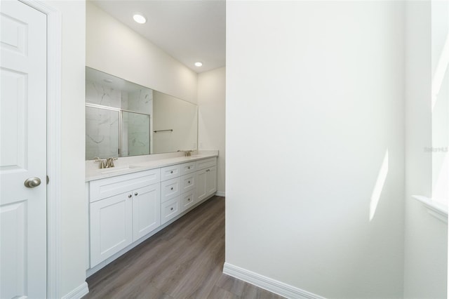 full bathroom featuring double vanity, wood finished floors, a sink, and a marble finish shower