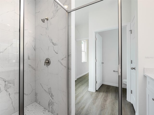 bathroom with toilet, vanity, a marble finish shower, and wood finished floors