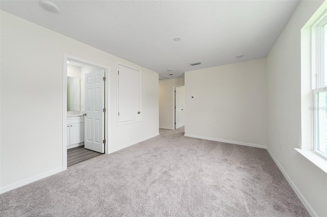 carpeted spare room with a textured ceiling, plenty of natural light, visible vents, and baseboards