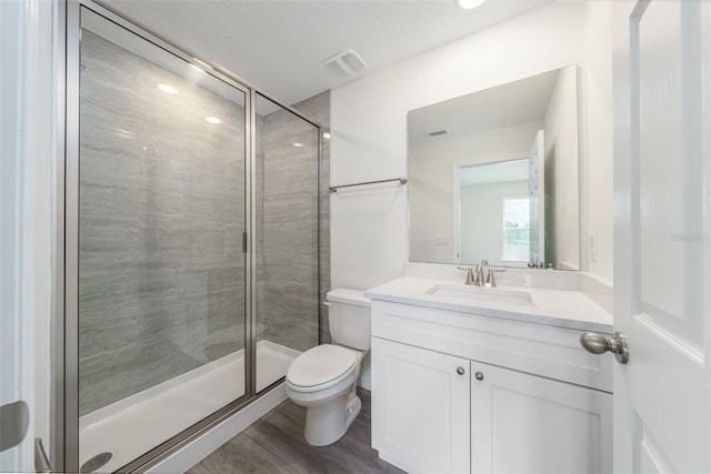 bathroom with visible vents, toilet, vanity, a shower stall, and wood finished floors