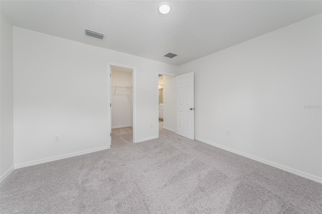 unfurnished bedroom with carpet floors, visible vents, a spacious closet, a textured ceiling, and baseboards